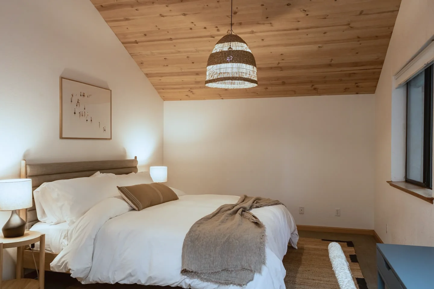 Sea Ranch bedroom under a vaulted wood ceiling with a woven pendant light