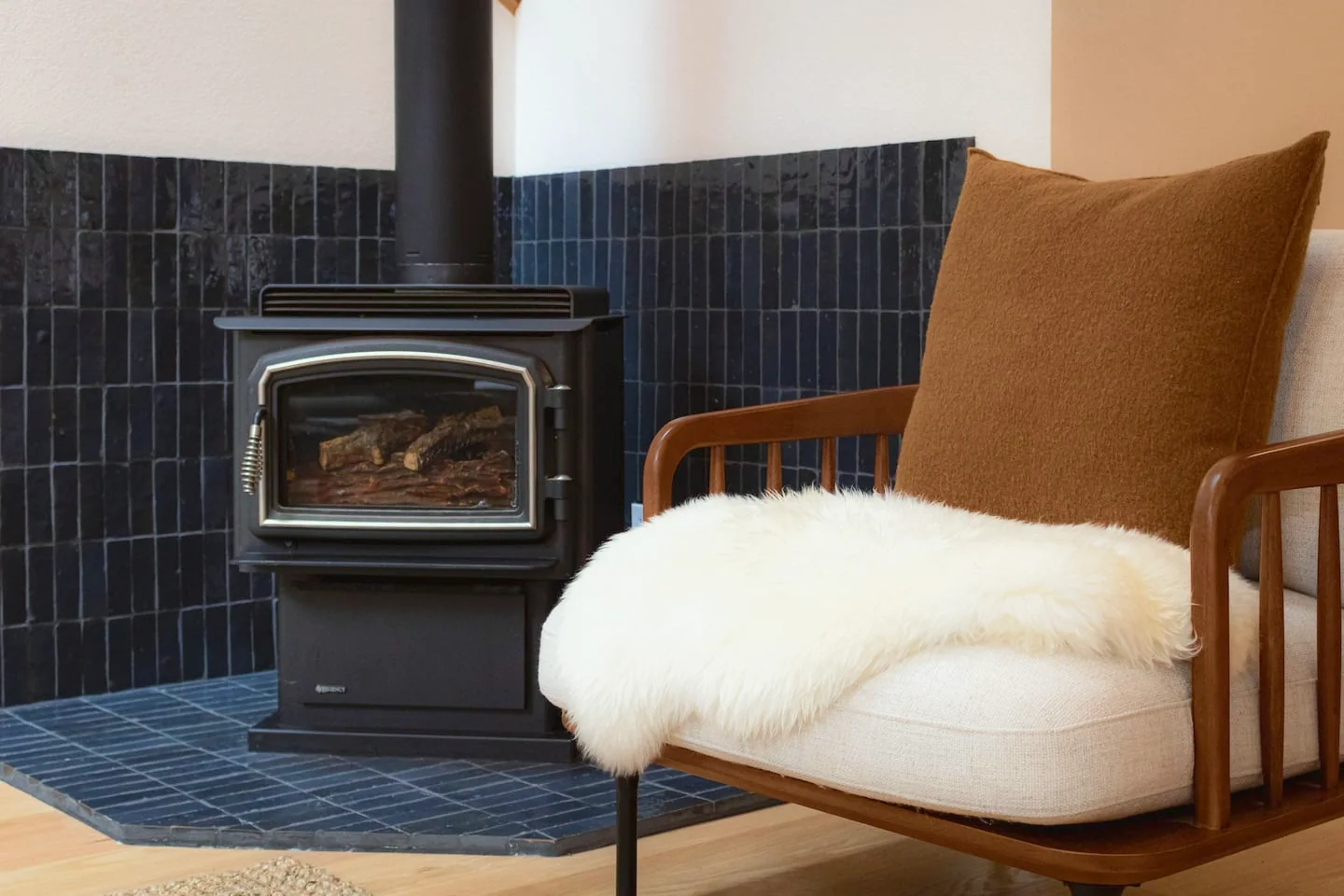 Wood stove against black tile, beside an armchair with a sheepskin throw